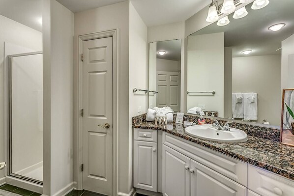 Une salle de bain avec une porte blanche, un lavabo doté d’un plan de travail en granit et un grand miroir au-dessus du lavabo.