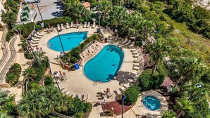 An aerial view of a resort with two large swimming pools surrounded by lounge areas and palm trees. - Margate Penthouse Myrtle Beach (Myrtle Beach)