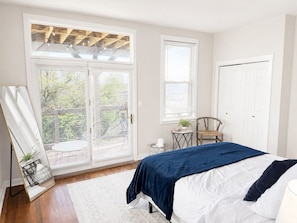 A bedroom with a bed, a chair, a small table, and a window with blinds.