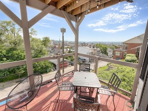 A covered outdoor patio with a table and chairs, a hammock, and a view of a residential area.