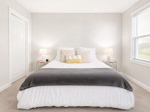 A bedroom with a bed, two bedside tables, a window, and a door.