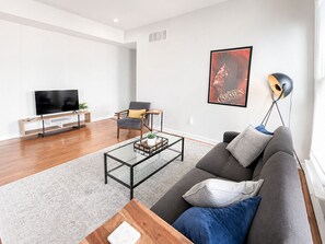 A modern living room with a sofa, coffee table, TV, and a poster on the wall. - Bright and Sweeping Views in OTR Treehouse (Cincinnati)
