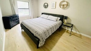Ein Schlafzimmer mit Bett, Kommode, Fenster mit Vorhängen und Wanddekoration.