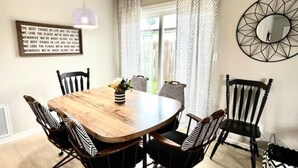 A dining area with a wooden table, black and white striped chairs, a hanging light fixture, and a decorative mirror on the wall.