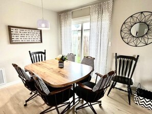 Un coin repas avec une table en bois, des chaises à rayures noires et blanches, un luminaire suspendu et un miroir décoratif accroché au mur.