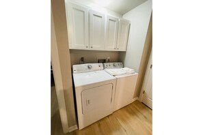 Compact laundry room with washer and dryer, featuring white cabinetry and a wooden floor.