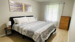 A bedroom with a bed, a nightstand, a dresser, and a window with curtains. - Live like a local in our cozy, clean home! (Fayetteville)