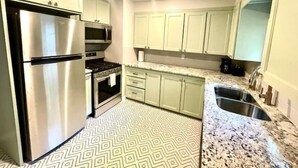 A kitchen with white cabinets, stainless steel appliances, a patterned floor, and granite countertops.