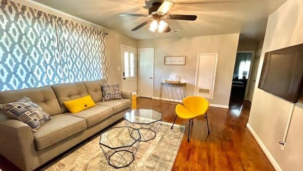 A living room with a sofa, a coffee table, and a yellow chair. There is a ceiling fan and a patterned wall.