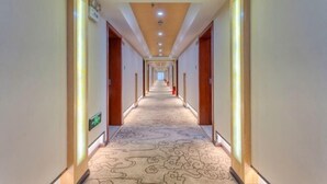 Un pasillo largo y bien iluminado con alfombra estampada y puertas de madera, que conduce a varias habitaciones.