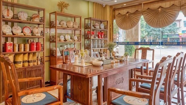Un restaurante con muebles de madera, estantes con vajilla y vista a la calle.