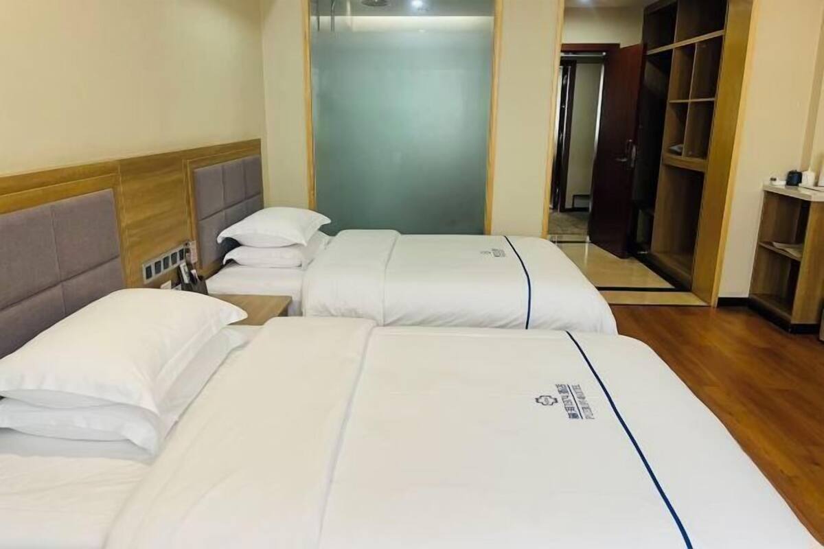 Une chambre d’hôtel avec deux lits, une armoire et une salle de bain visible à travers une porte en verre.