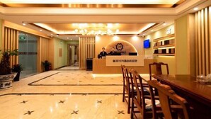 Vestíbulo de hotel con mostrador de recepción, una araña de cristal, suelo de mármol y sillas de madera.