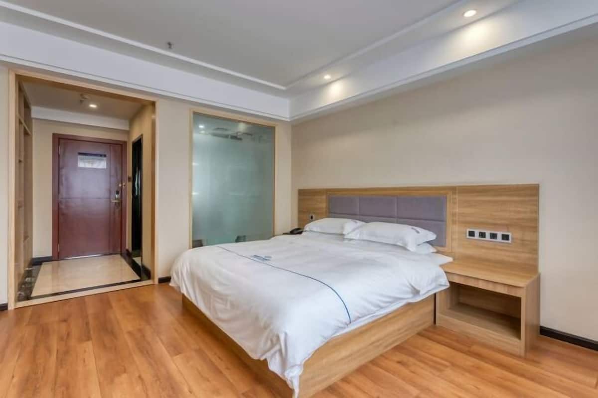 Une chambre d’hôtel moderne avec un plancher en bois, un lit doté d’une tête de lit, une table de chevet et une porte donnant sur une autre pièce.