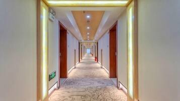 Un largo y estrecho pasillo de hotel con alfombra estampada, puertas de madera e iluminación empotrada en el techo.