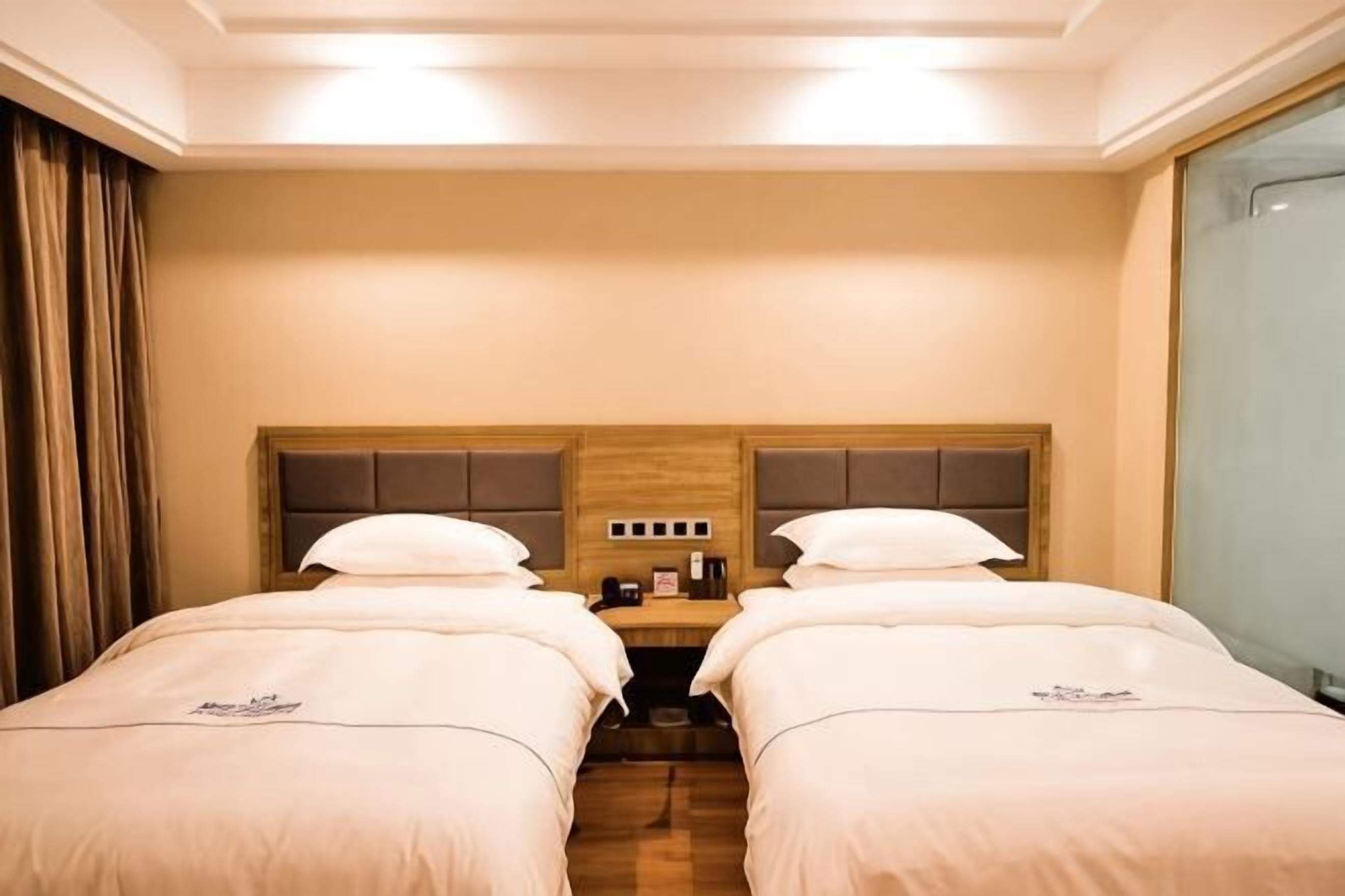 Une chambre d’hôtel avec deux lits, une tête de lit en bois, une petite table avec une machine à café et une fenêtre avec des rideaux.