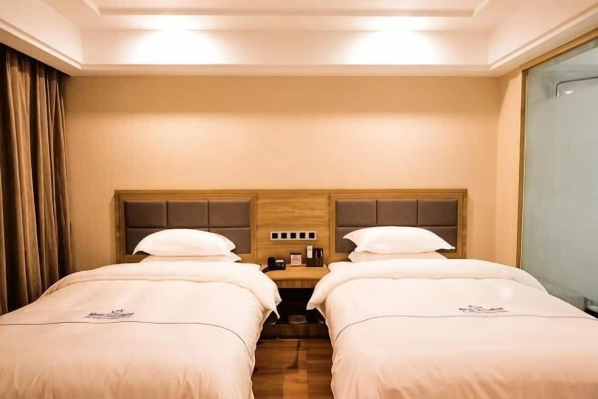 Une chambre d’hôtel avec deux lits, une tête de lit en bois, une petite table avec une machine à café et une fenêtre avec des rideaux.