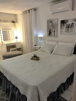Un dormitorio ordenado con cama, mesitas de noche, tocador con espejo y obras de arte en las paredes.
