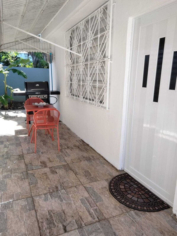 Un patio couvert équipé d’un barbecue, de meubles d’extérieur et d’une porte blanche.
