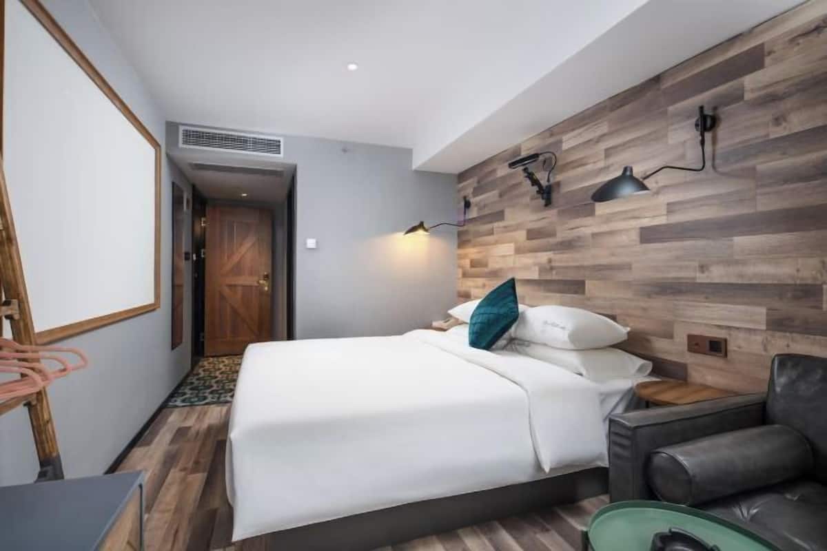 Ein Schlafzimmer mit einem Bett, einem Schreibtisch, einem Sessel und einer Wandleuchte.
