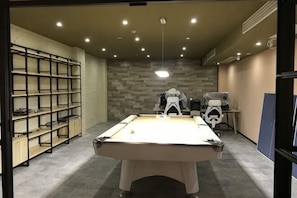 Ein Billardtisch in einem Raum mit Regalen, einem Stuhl und einer Wand mit Musterdesign.