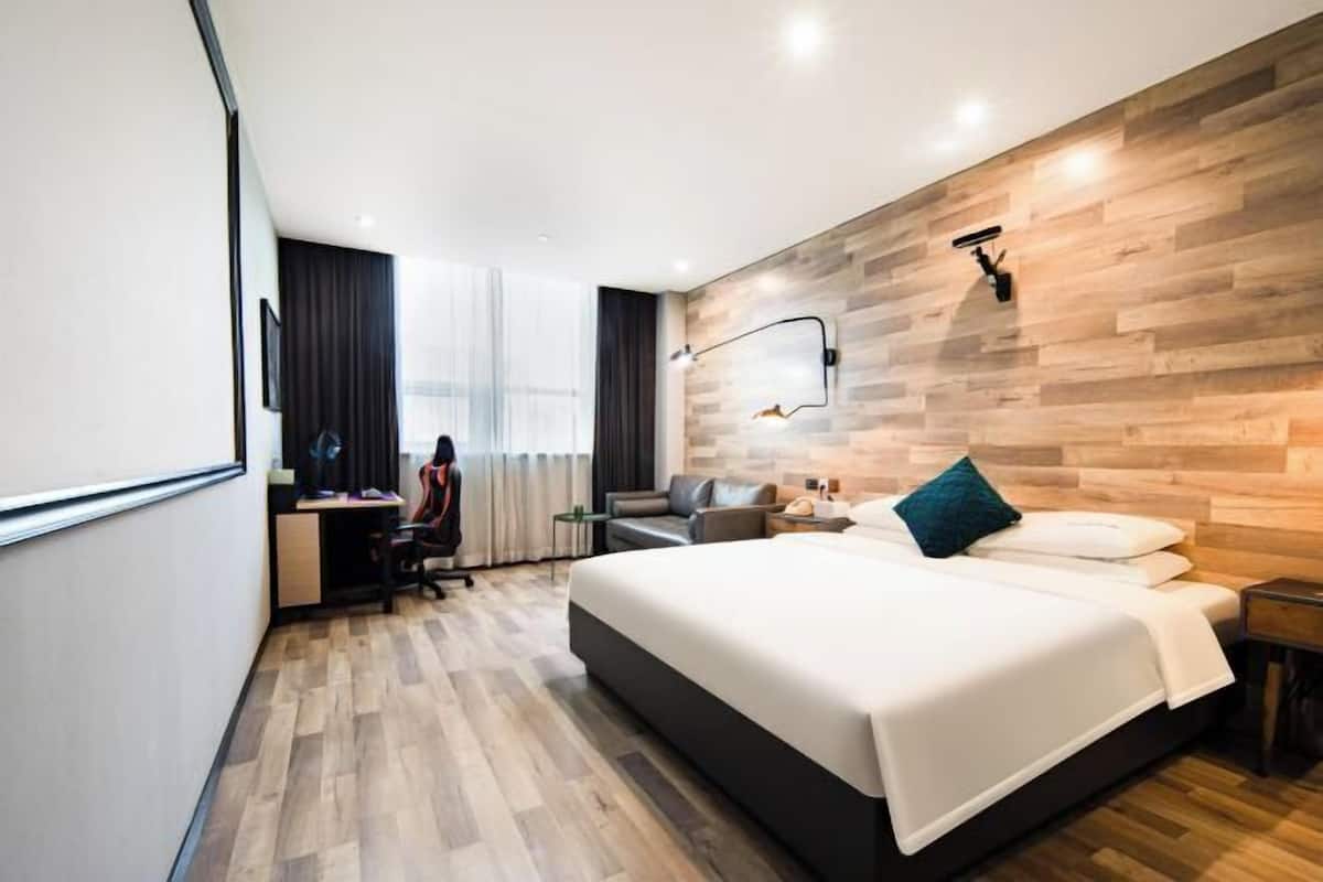 Ein modernes Hotelzimmer mit einem großen Bett, einem Schreibtisch mit Stuhl, einer Couch und einer Wandlampe.