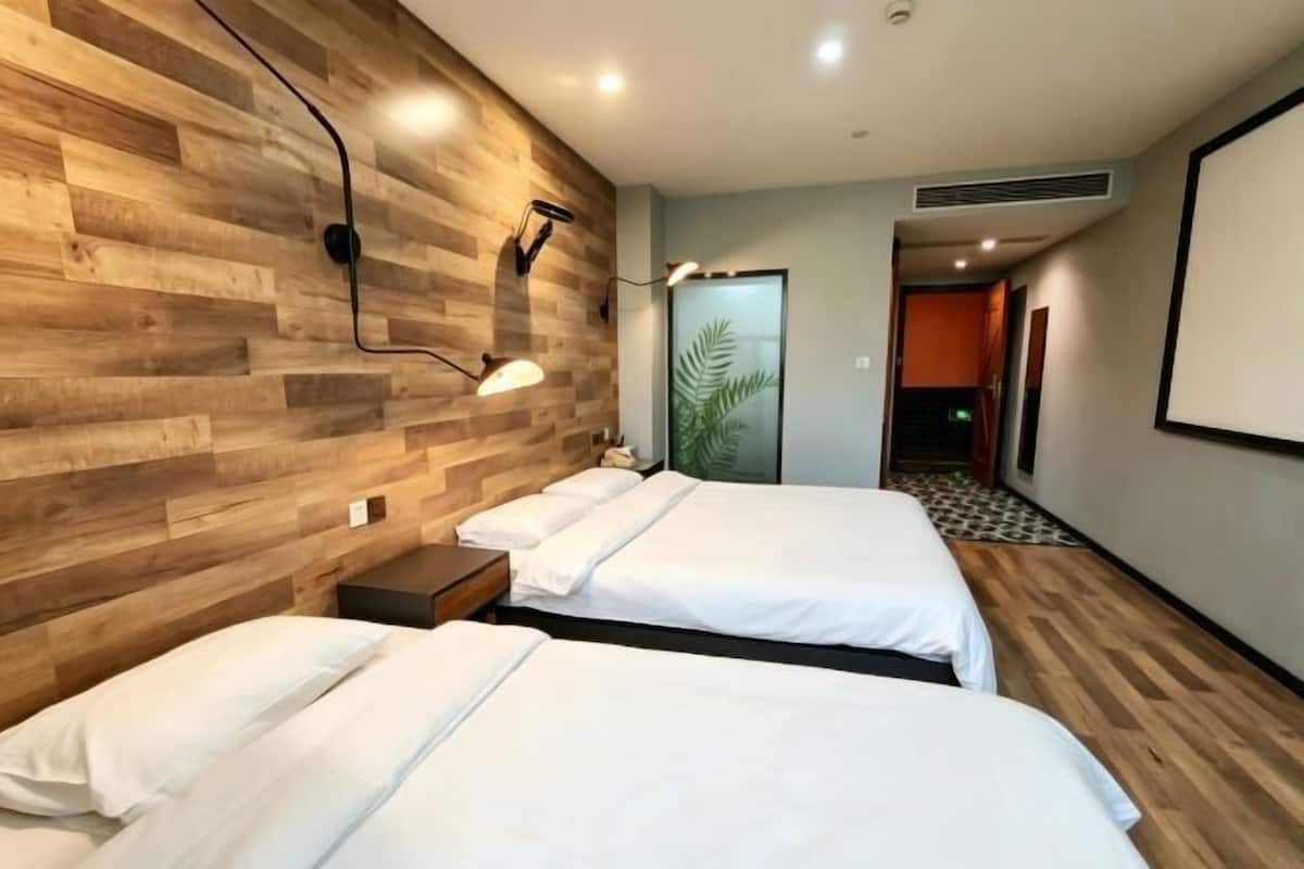 Ein Hotelzimmer mit zwei Betten, Holzvertäfelung, einem Nachttisch, einer Wandlampe und einer Tür zu einem weiteren Raum.