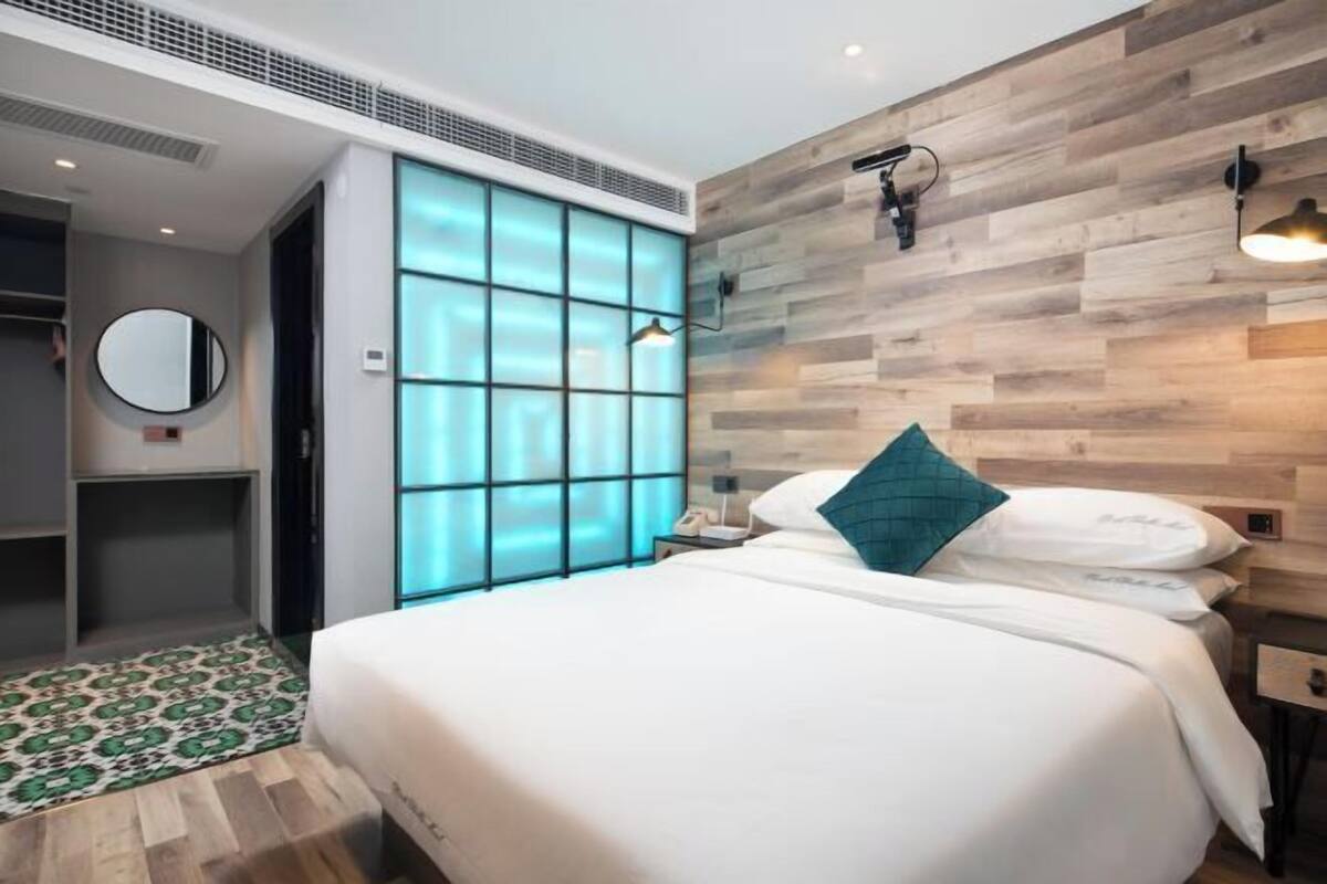 Ein modernes Hotelzimmer mit einem großen Bett, einer Wand mit Holzapplikationen, einem kleinen Nachttisch, einem Beistelltisch, einem Spiegel und einem gemusterten Teppich.