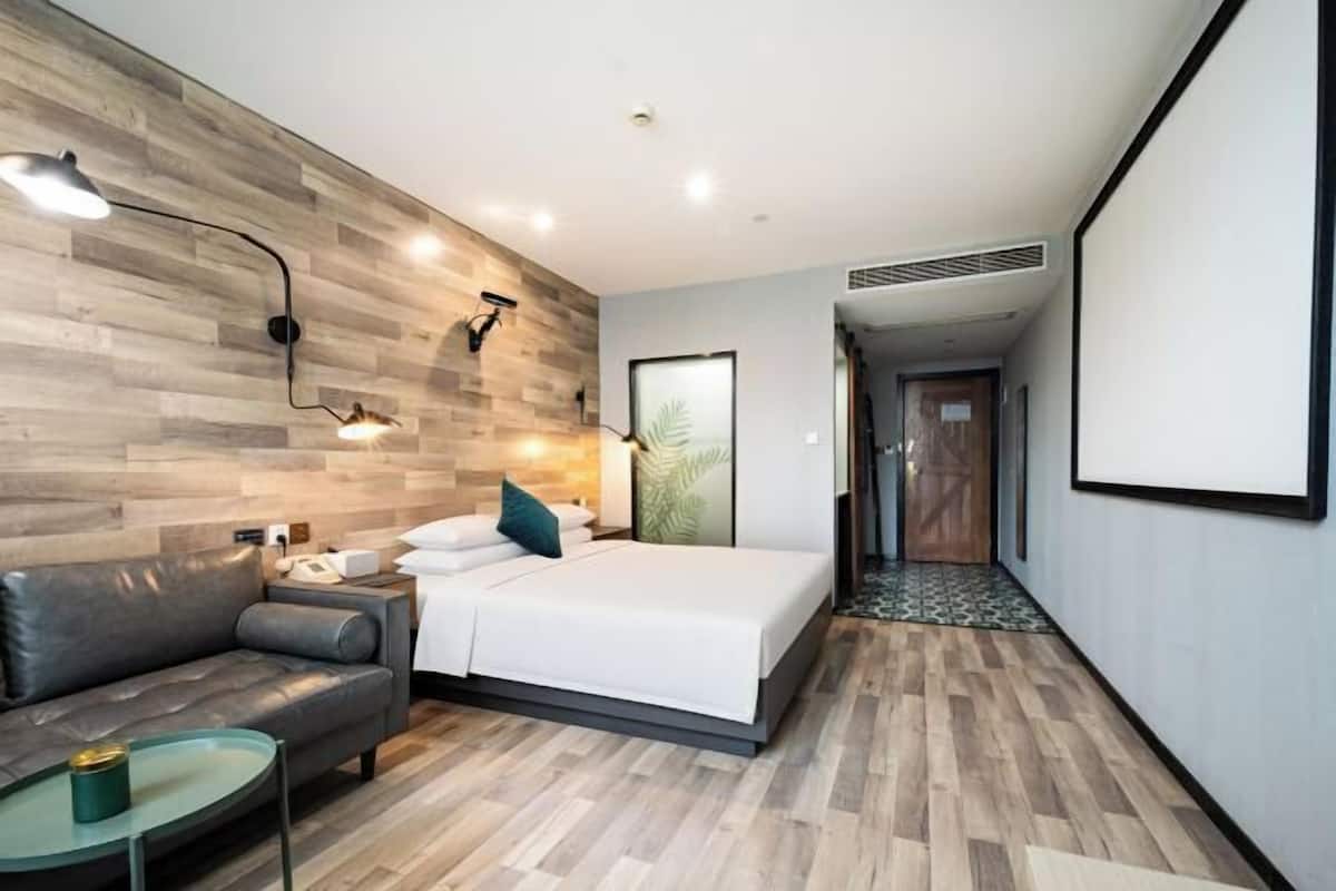 Ein modernes Hotelzimmer mit einer Holzwand, einem Bett, einem Sofa, einem Nachttisch und einer Lampe.