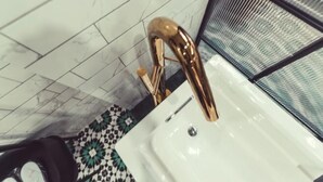 Un baño con lavamanos blanco, grifo dorado y piso estampado.