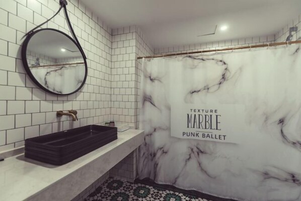 Un baño con cortina de ducha de textura de mármol, un espejo redondo y un lavabo negro.