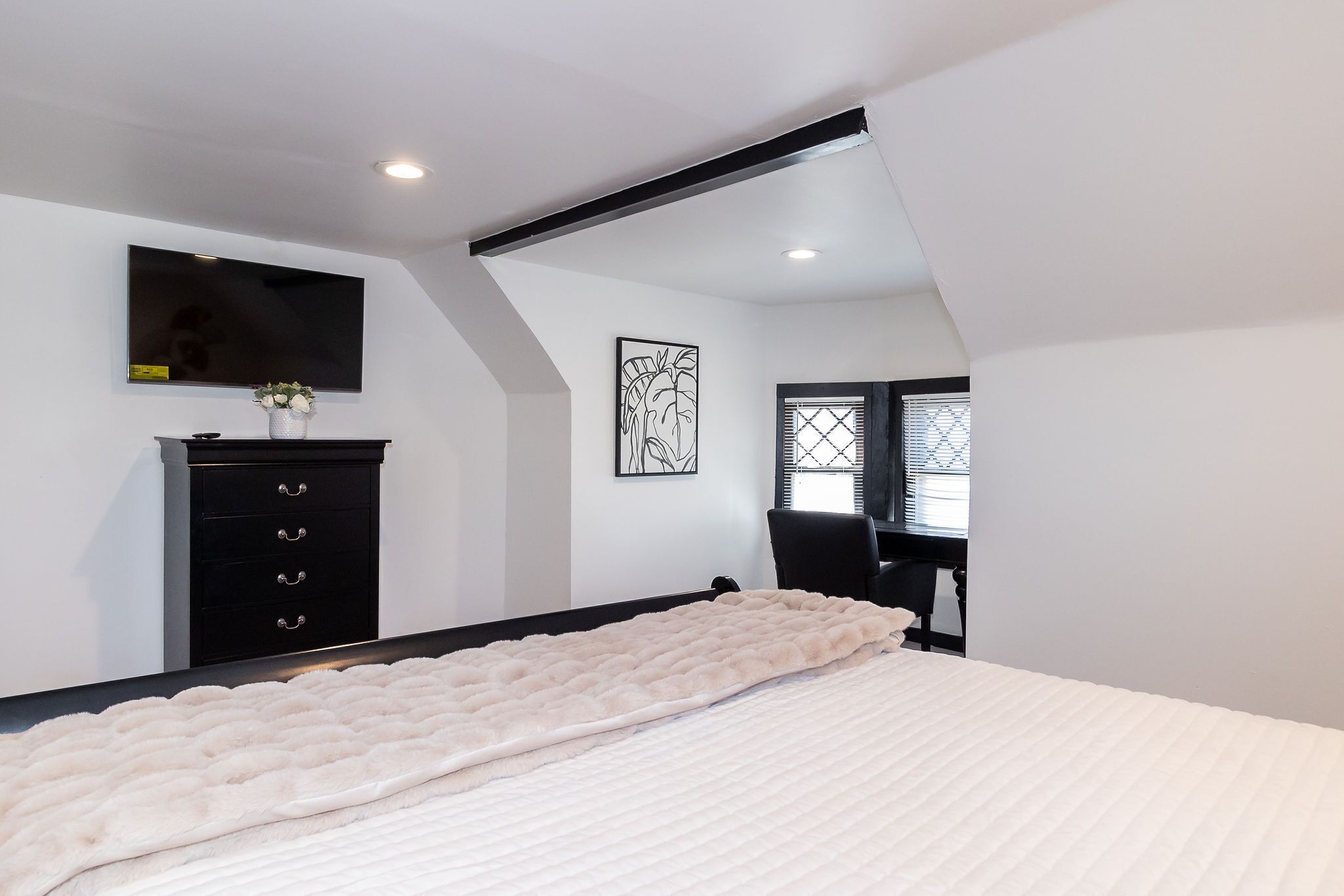 Un dormitorio con cama, cómoda, televisor y ventana con persianas.