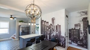 A modern kitchen with a built-in island, a dining area with a black table, and a cityscape mural on the wall. - Home Detroit Beautiful Historic  (Detroit)