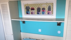Quarto com paredes verde-água, cama com cobertura azul listrada, janela com arte temática de cactos e móveis brancos.