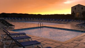 Piscina com espreguiçadeiras e um edifício ao fundo.