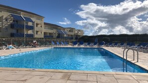 Piscina com espreguiçadeiras e um edifício com varandas.