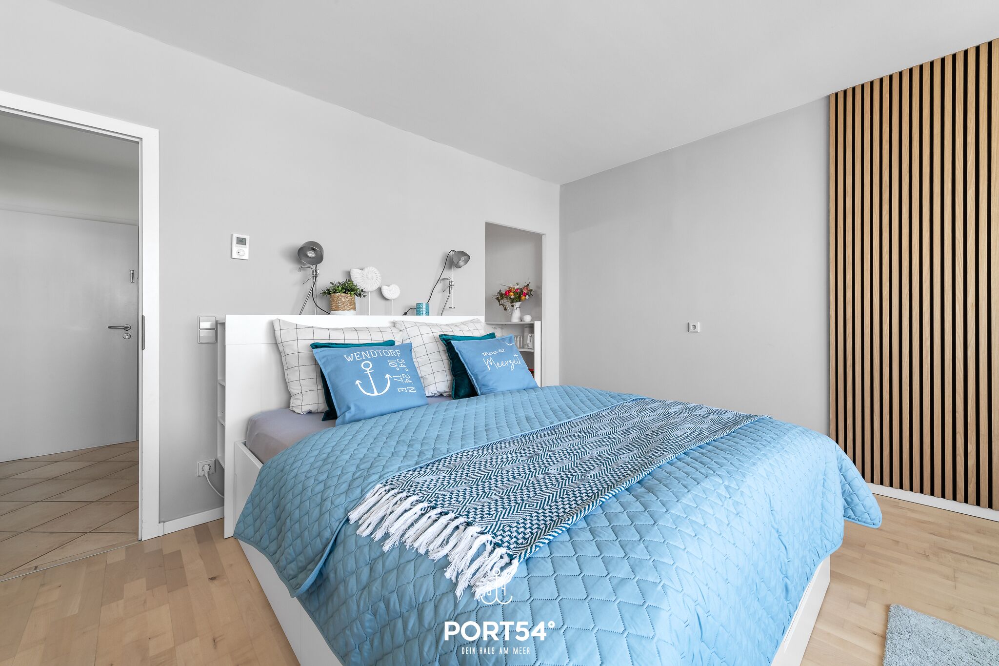 A modern bedroom with a bed, a bedside table, a wall-mounted shelf, and a wooden slat wall panel.