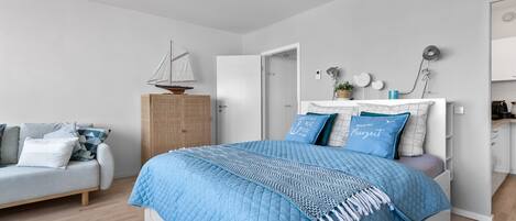 Un dormitorio moderno con una cama grande, un armario de madera, una pequeña decoración de velero y una zona de kitchenette.