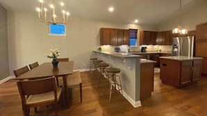 A spacious kitchen with wooden cabinets, a central island, and a dining area with a table and chairs. - Modern Luxury | Steps to Brady St (Milwaukee)