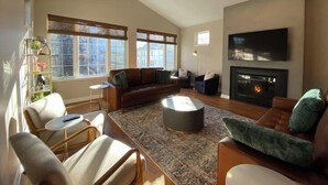 A spacious living room with a fireplace, a ceiling fan, and large windows providing natural light. - Modern Luxury | Steps to Brady St (Milwaukee)