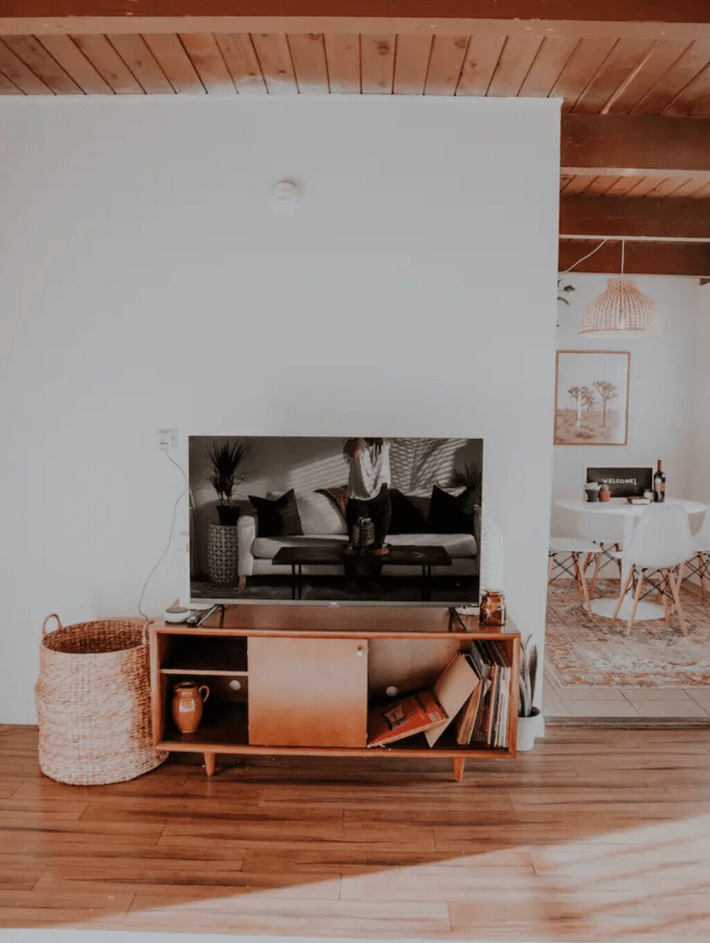 A modern living room with a wooden floor, a TV on a wooden stand, a white sofa, a coffee table, and a dining area with a table and chairs.