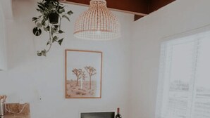 Un coin repas avec une table ronde, quatre chaises blanches, une pancarte « BIENVENUE », une bouteille de vin et une plante suspendue.