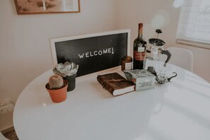 Een ronde tafel met een welkomstbord, een fles wijn, een theepot, een boek, een kleine cactus en een pak koffie.