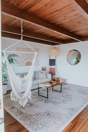 Une pièce chaleureuse avec un hamac, un miroir rond et un plafond en bois.