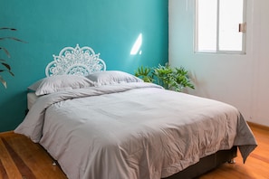 Een bed met een wit hoofdeinde en grijze beddengoed in een kamer met teal muren en houten vloeren.