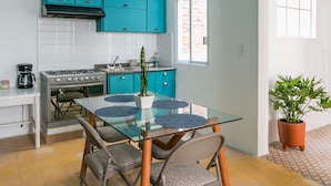 A compact kitchen with teal cabinets, a gas stove, and a dining area with a glass table and chairs. - Acogedor y Amplio Departamento Roma Nte (Mexico City)