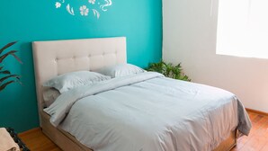 A neatly made bed with a light-colored headboard and bedding, a wooden floor, and a teal wall with a floral decal. - Acogedor y Amplio Departamento Roma Nte (Mexico City)