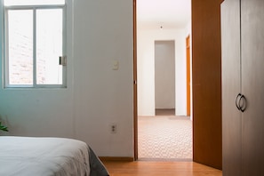 Een kamer met een bed, een houten kledingkast, een raam en een deur naar een andere kamer.