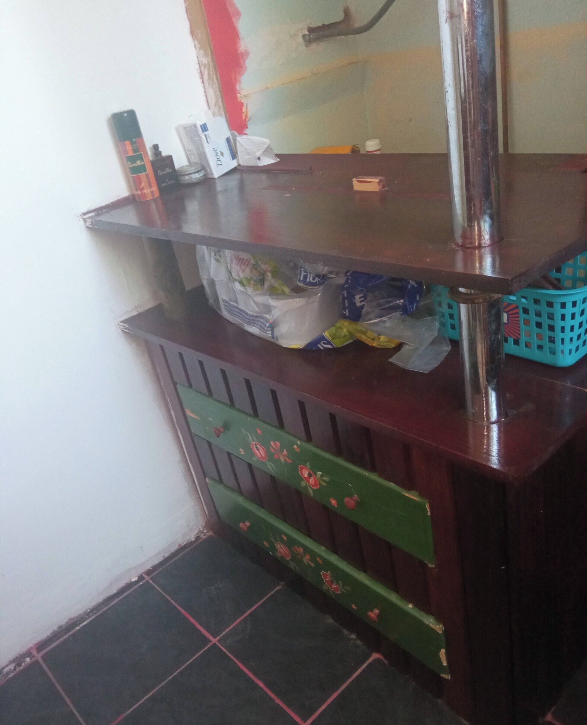 A wooden counter with a mirror, various items on top, and a green drawer with floral patterns.