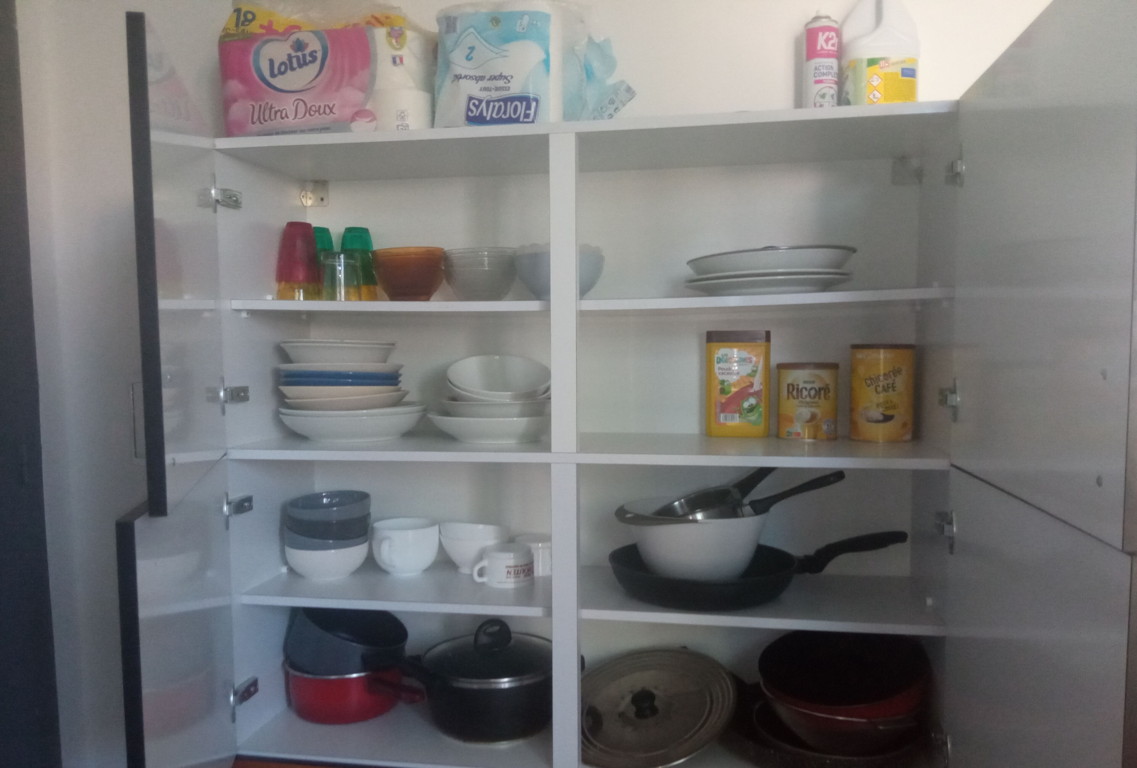 A kitchen pantry with shelves stocked with bowls, cups, and cooking pots.